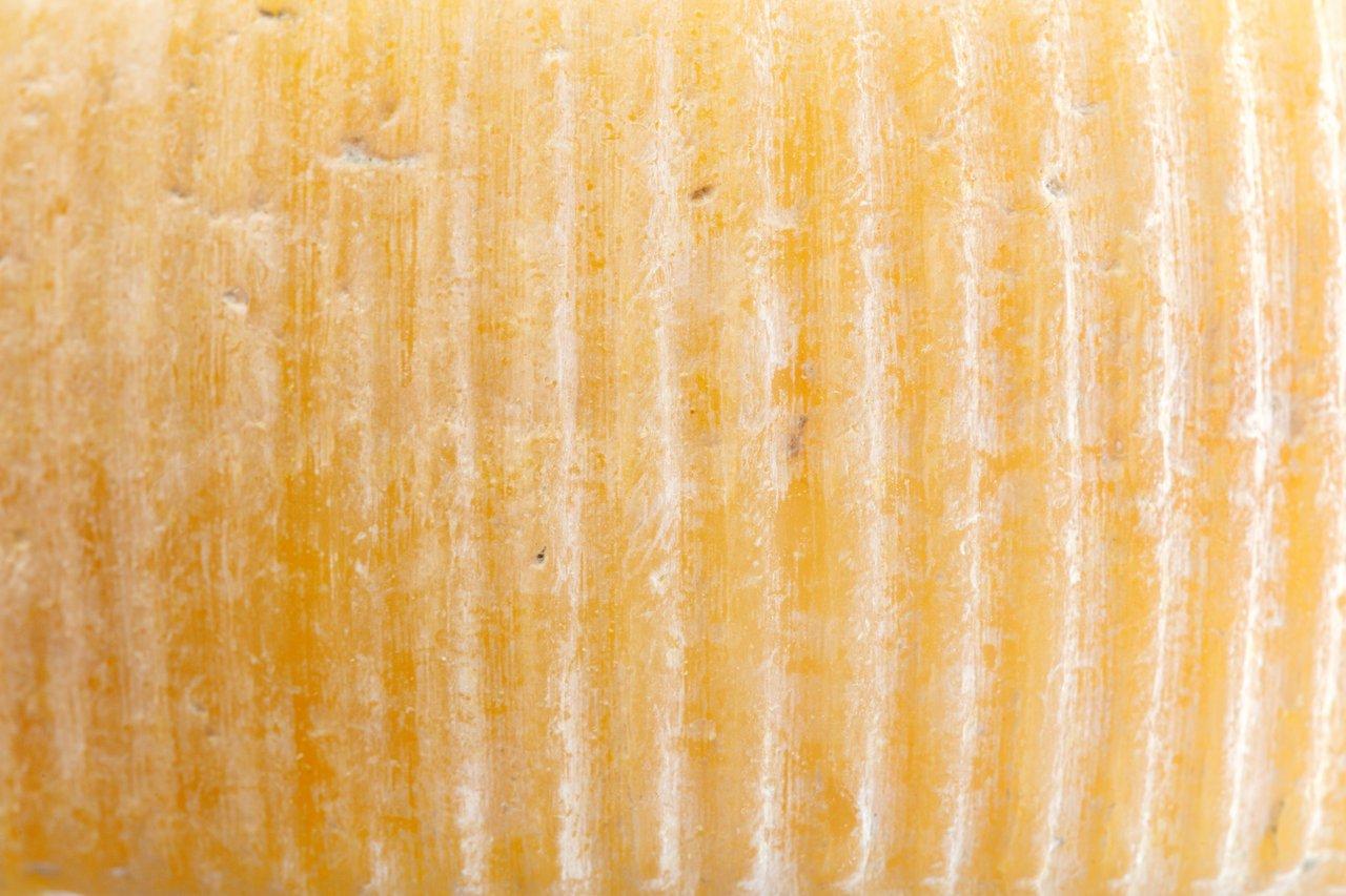 Détail en gros plan d’un fromage Pont-l’Évêque carré à croûte lavée, aux dégradés de couleurs du blanc au rougeâtre.
