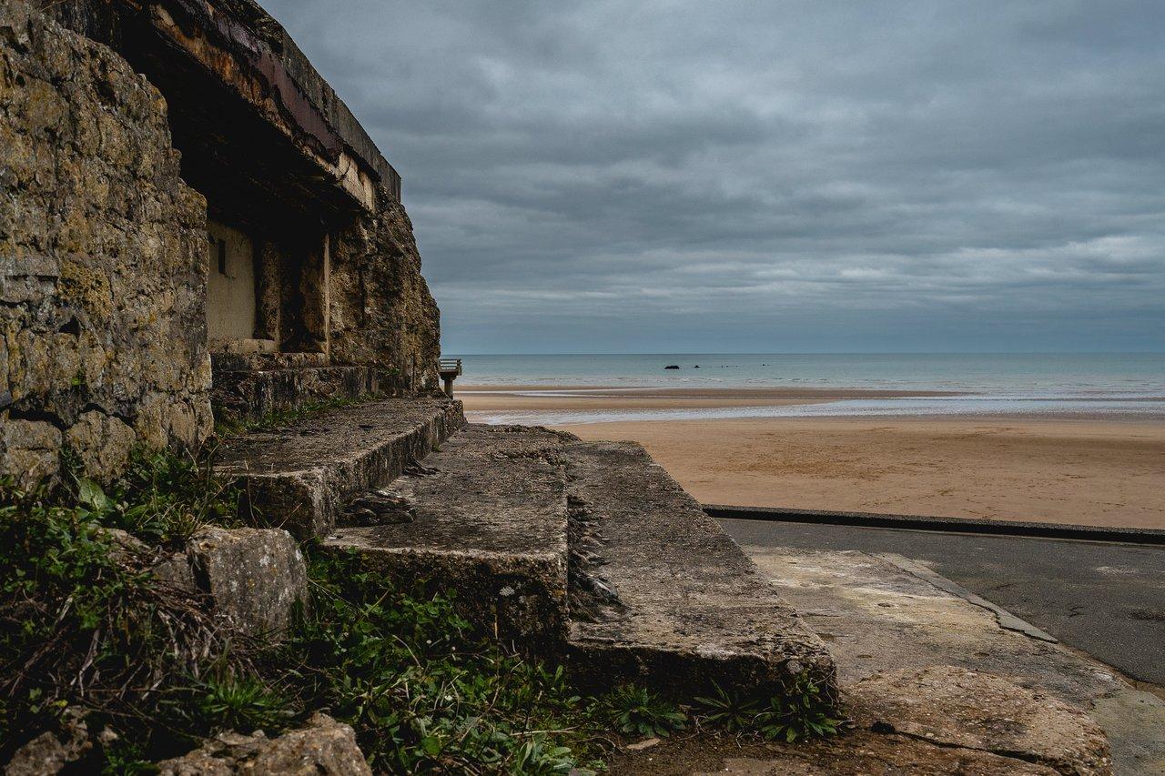 Panorama d'Omaha Beach avec dunes, cimetière américain et randonneur sur le sentier côtier en Normandie.